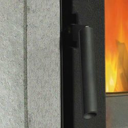 The image shows a section of a wood-burning stove with a clear focus on the door and handle. The fiery flames in the background radiate a welcoming warmth, and the solid handle ensures safe handling. The stove is partially clad in stone, giving the design an elegant and stylish look. Perfect for modern living spaces and cozy evenings in front of the wood-burning stove.