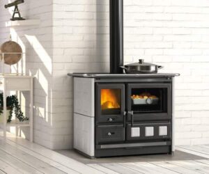 The picture shows a stylish wood-burning stove in a bright room. The stove has elegant white tile cladding and a large viewing window through which you can easily watch the flames dance. Next to it is an oven, which makes the wood-burning stove particularly multifunctional. The wood-burning stove radiates cozy warmth and is an attractive addition to any home. Perfect for anyone who values design and efficiency.