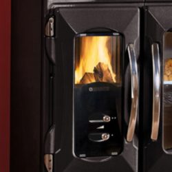 The image shows a detailed section of a wood-burning stove, specifically the glass viewing panel. The panel allows you to see the lively flames of the wood-burning stove, which creates a cozy atmosphere. The shiny metal handles and stylish black design emphasize the modern aesthetics of the stove. Perfect for enjoying the warmth and atmosphere of a wood-burning stove.