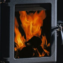 De afbeelding toont een gedetailleerd fragment van een houtkachel, met de nadruk op de vuurplaat. Achter de glasplaat laaien levendige vlammen op, die een warme en uitnodigende sfeer creëren. De robuuste metalen rand van de houtkachel geeft het ontwerp een stijlvolle en tijdloze uitstraling. Ideaal als aanvulling op een gezellige woonkamer met een houtkachel.