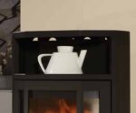 De afbeelding toont een zwarte houtkachel, of beter gezegd een deel van de kachel met een detailfocus op het bovenste gedeelte. Daarop staat een witte keramische of porseleinen kruik. De houtkachel is gemaakt van staal en heeft een eenvoudige, moderne uitstraling die goed past bij eigentijdse interieurontwerpen. Perfect voor iedereen die zijn woonruimte wil verwarmen met een stijlvolle en functionele houtkachel.