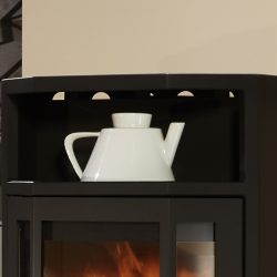 De afbeelding toont een zwarte houtkachel, of beter gezegd een deel van de kachel met een detailfocus op het bovenste gedeelte. Daarop staat een witte keramische of porseleinen kruik. De houtkachel is gemaakt van staal en heeft een eenvoudige, moderne uitstraling die goed past bij eigentijdse interieurontwerpen. Perfect voor iedereen die zijn woonruimte wil verwarmen met een stijlvolle en functionele houtkachel.