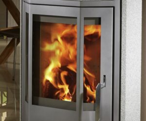 The picture shows a detailed section of a wood-burning stove with gray natural stone. The focus is on the glass pane, through which lively flickering flames can be seen. The stove combines modern design with a traditional heat source and radiates elegance and coziness. Ideal for any home looking for a wood-burning stove with aesthetic natural stone.