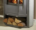 The picture shows a gray stove with natural stone elements. The focus is on the lower section, where there is a wood compartment filled with several logs. The stove offers an attractive combination of modern design and practical wood storage, ideal for a cozy ambience.