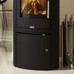 De afbeelding toont een detail van een houtkachel, waarbij de focus ligt op een specifiek onderdeel van de kachel. De houtkachel heeft een helder kijkvenster waardoor de laaiende vlammen zichtbaar zijn. Daaronder bevindt zich een gladde, donkere frontplaat. Rechts naast de kachel is een glanzende houtkachel-gereedschapshouder te zien. Deze detailafbeelding benadrukt de elegante afwerking en het rustgevende vlammenspel in de houtkachel.