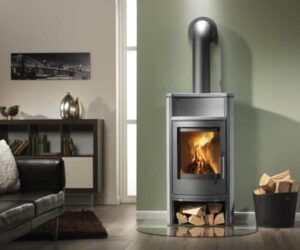 A stylish wood-burning stove in a modern soapstone design is the focal point of a cozy living room. The stove is elegant and functional with a visible wood compartment at the bottom that provides practical access to firewood. An inviting fire blazes in the stove behind a clear glass panel, radiating warmth and coziness. This soapstone wood stove is not only an eye-catcher, but also a sustainable source of heat, ideal for stylish living spaces.