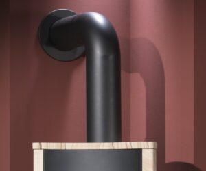 Das Bild zeigt ein Ofenrohr in einem Kaminofen Online Shop. Das schwarze Ofenrohr ist in einem eleganten Winkel installiert und geht in die Wand über. Es ist oberhalb eines Holzofens platziert, wobei der obere Rand des Ofens sichtbar ist. Die matte Oberfläche des Ofenrohrs fügt sich harmonisch in die Umgebung ein und unterstreicht die Funktionalität und Ästhetik des Kaminofens. Dieses Detail ist essenziell für die effiziente Abführung von Rauch und Wärme.