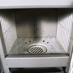 De afbeelding toont het interieur van een houtkachel, meer bepaald de binnenkant van de verbrandingskamer van het model Rossella Plus. De focus ligt op de robuuste bekleding van de verbrandingskamer met hittebestendige materialen. In het onderste gedeelte bevindt zich een rooster voor de afvoer van as, dat zorgt voor een efficiënte verbranding in de houtkachel. Dit onderdeel van de kachel is belangrijk voor een gelijkmatige warmteverdeling en een langdurig gebruik. Ideaal voor iemand die op zoek is naar een betrouwbare en hoogwaardige kachel.