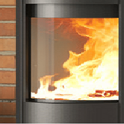 De afbeelding toont de glazen ruit van een elegante open haard, waardoor het laaiende vuur levendig te zien is. De vlammen dansen achter de heldere ruit, wat een warme en uitnodigende sfeer creëert. Dit fragment benadrukt de kwaliteit en transparantie van de ruit, terwijl het indrukwekkende effect van het vuur in een moderne houtkachel wordt getoond. Perfect voor elke stijlvolle woonkamer.