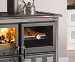 The image shows a section of a wood-burning stove that specifically highlights the baking compartment. On the left-hand side, you can see the flames in the stove, and on the right-hand side, the baking compartment where food can be cooked. The modern, elegant surface of the stove gives the room a stylish look. Perfect for anyone looking for a multifunctional wood-burning stove that not only provides heat but also serves as a baking oven.