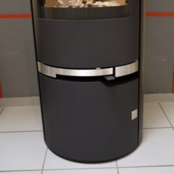 De afbeelding toont het onderste deel van een moderne houtkachel, met name het handvatdetail van het model "Filou II HL". De focus ligt op het elegante, metalen handvat, dat goed past bij de rest van het zwarte ontwerp van de houtkachel. De kachel staat op een lichte tegelvloer en de strakke lijnen onderstrepen het eigentijdse ontwerp. Deze kachel is perfect voor elk stijlvol interieur en biedt een praktische en esthetische oplossing voor behaaglijke warmte.