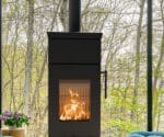 Moderner schwarzer Kaminofen mit großen Glastüren, durch die Flammen sichtbar sind, im Vordergrund eines Waldhintergrundes.