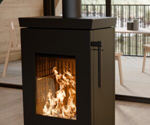 Feuer im Kaminofen Thermorossi Zen W, Fokus auf die Glasscheibe mit Blick auf die Flammen. Moderner Innenraum im Hintergrund.