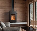 Kaminofen Thermorossi Zen W in modernem Wohnzimmer, eingebaut in eine Holzwand. Flammen sichtbar durch die Glasscheibe, gemütliche Atmosphäre.