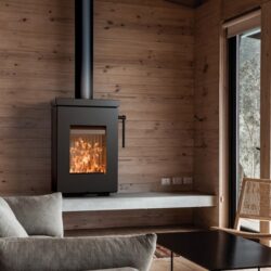 Kaminofen Thermorossi Zen W in modernem Wohnzimmer, eingebaut in eine Holzwand. Flammen sichtbar durch die Glasscheibe, gemütliche Atmosphäre.
